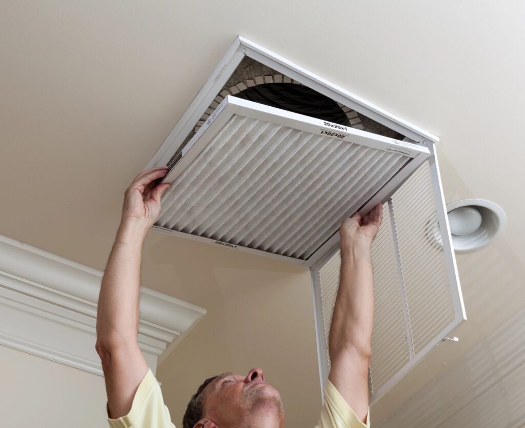 Person reaching up to change an air filter in a ceiling vent, like a pro from "AC repair near me" ads.